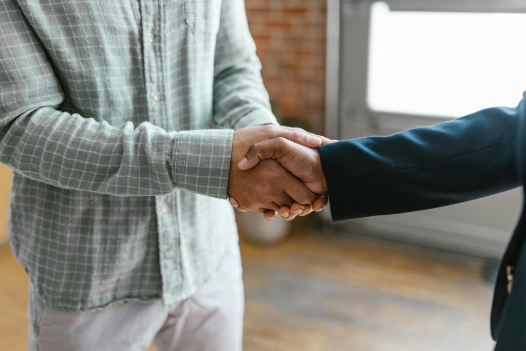 A Person in Green Plaid Long Sleeve Shirt Shaking Hands with Person in Black Blazer.